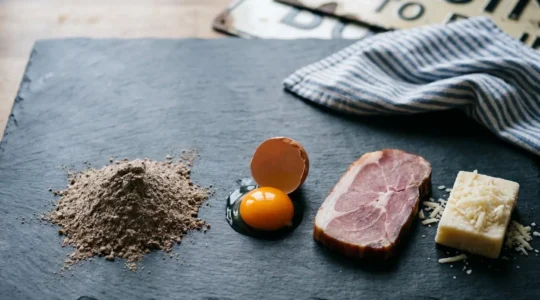 Composition élégante des quatre ingrédients essentiels d'une galette complète bretonne posés sur une table en ardoise